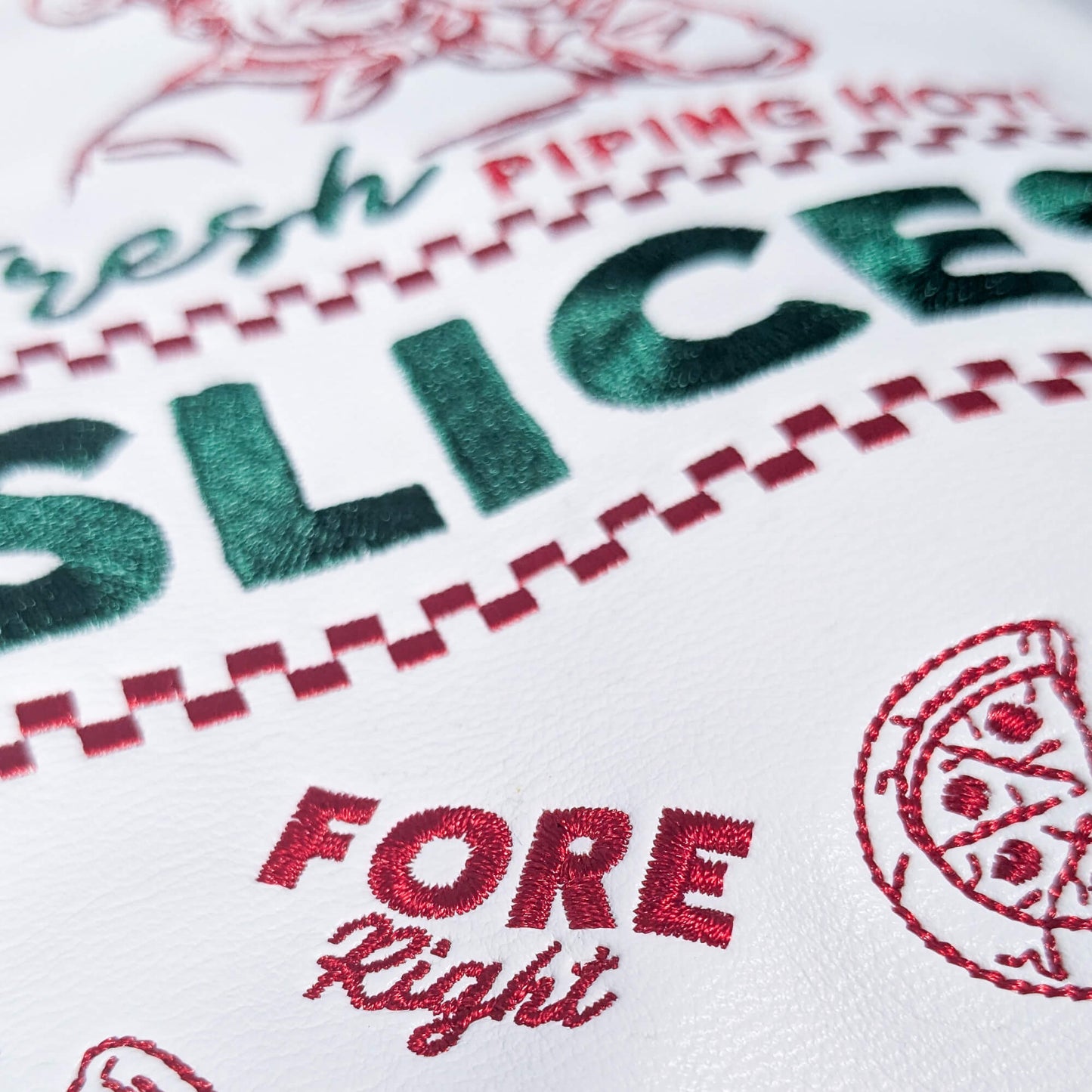 Embroidered text and design on a white fabric with red and green accents, featuring the word 'SLICES' and a pizza icon.