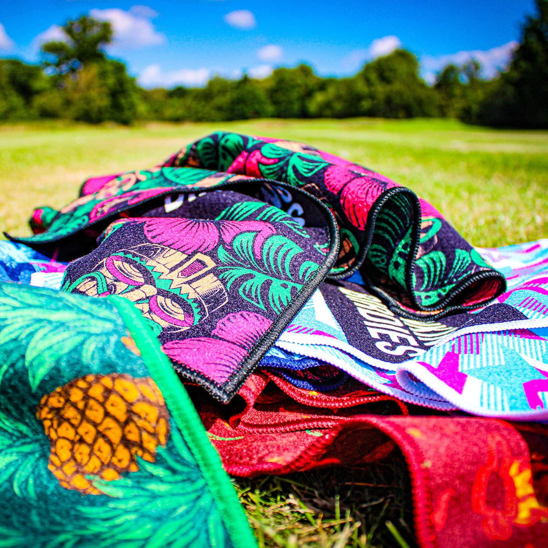 A close up of 5 patterned golf towels on a  piled on top of each other on a golf course