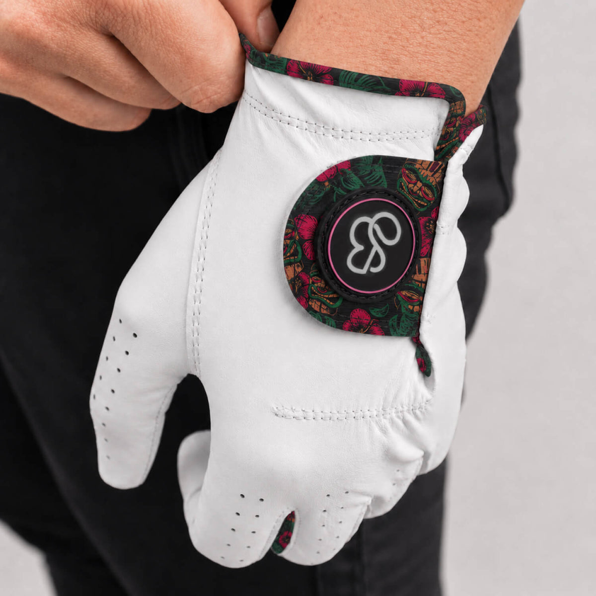 A close-up of a person wearing a white golf glove with a colorful paisley-patterned cuff and a circular logo patch on the back of the hand.