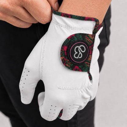A close-up of a person wearing a white golf glove with a colorful paisley-patterned cuff and a circular logo patch on the back of the hand.